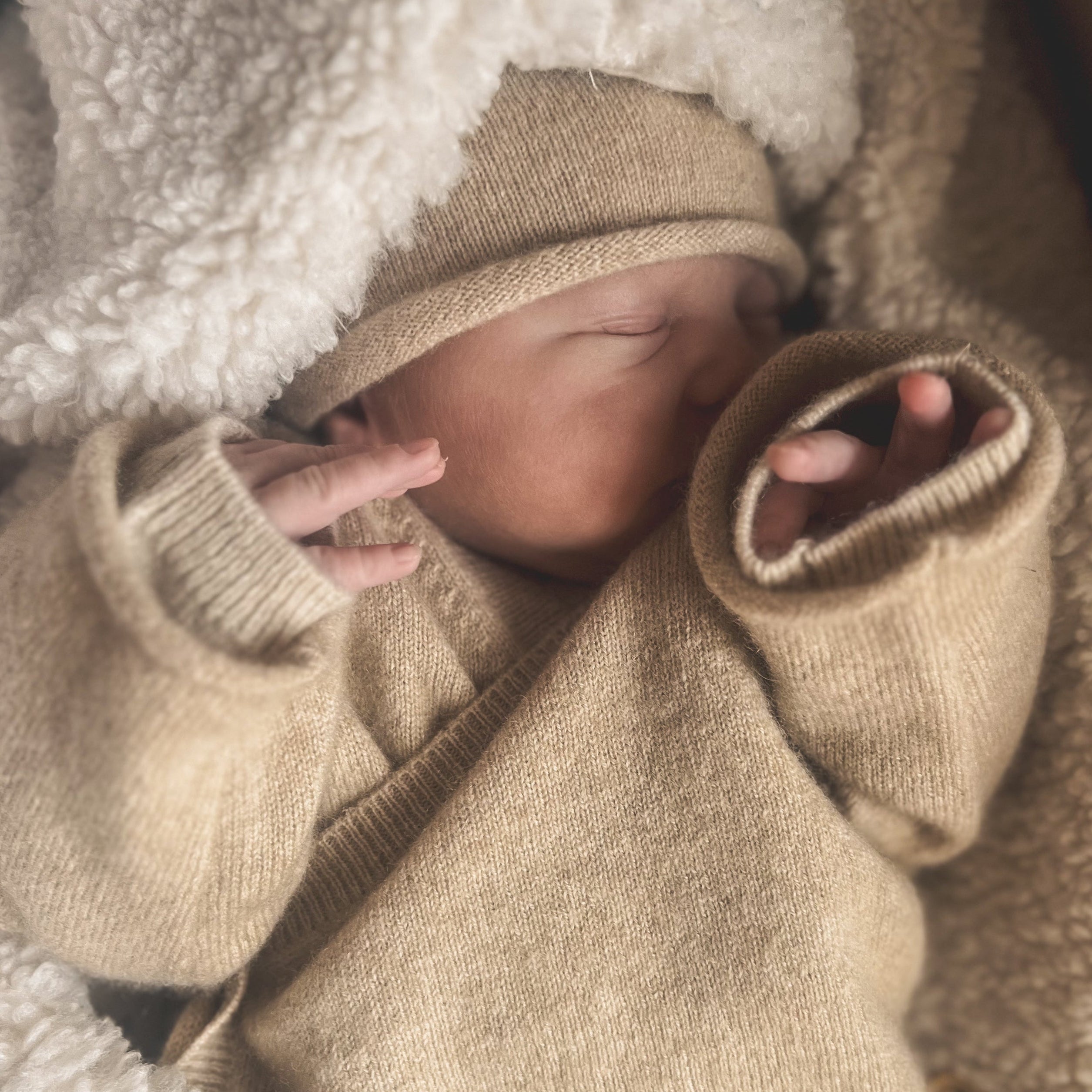 Newborn baby wrapped in a beige blanket and hat, sleeping peacefully.